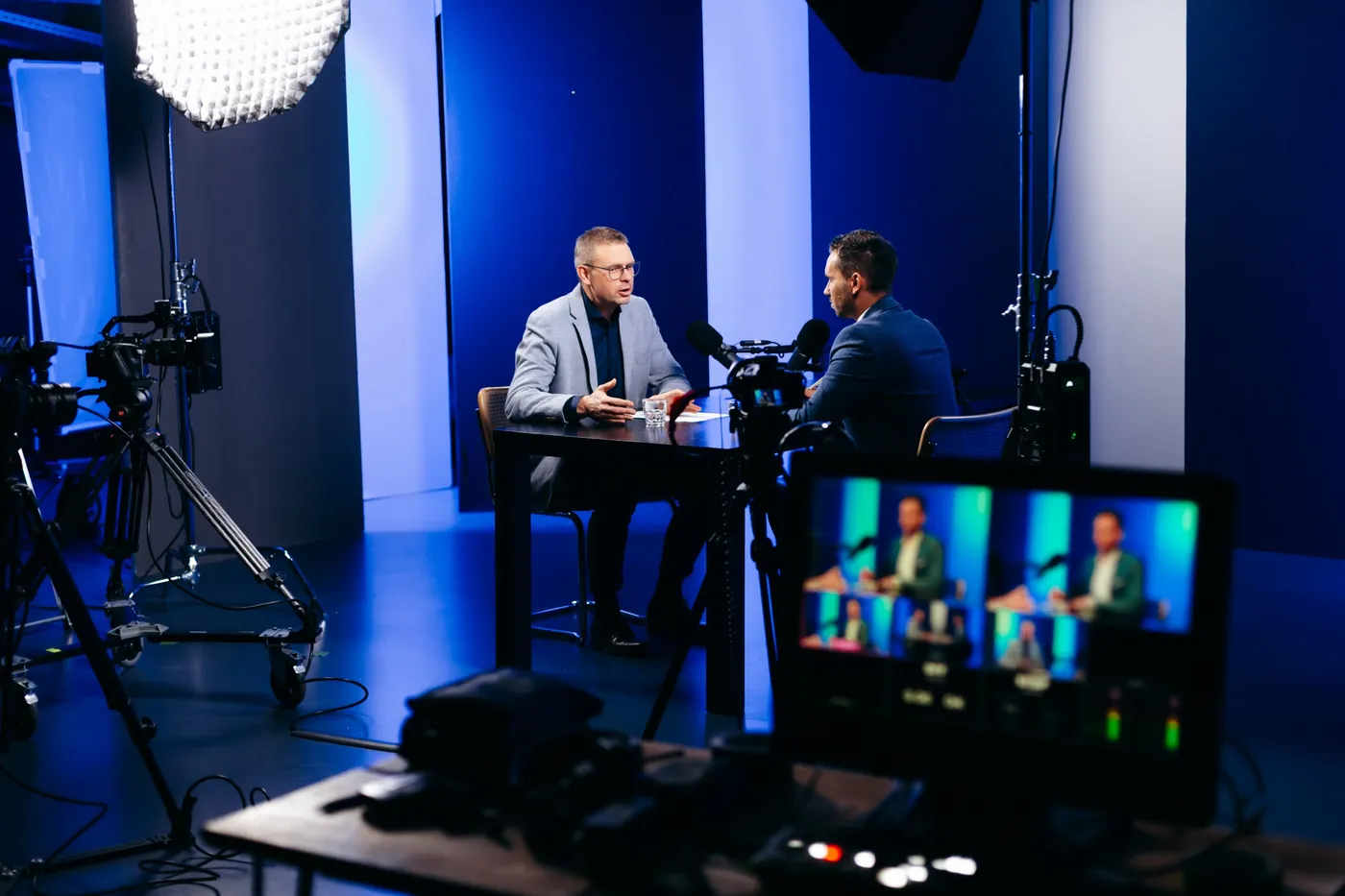 Interviewdreh im Studio: zwei Männer im Gespräch am Tisch, im Vordergrund Kamera und Monitor