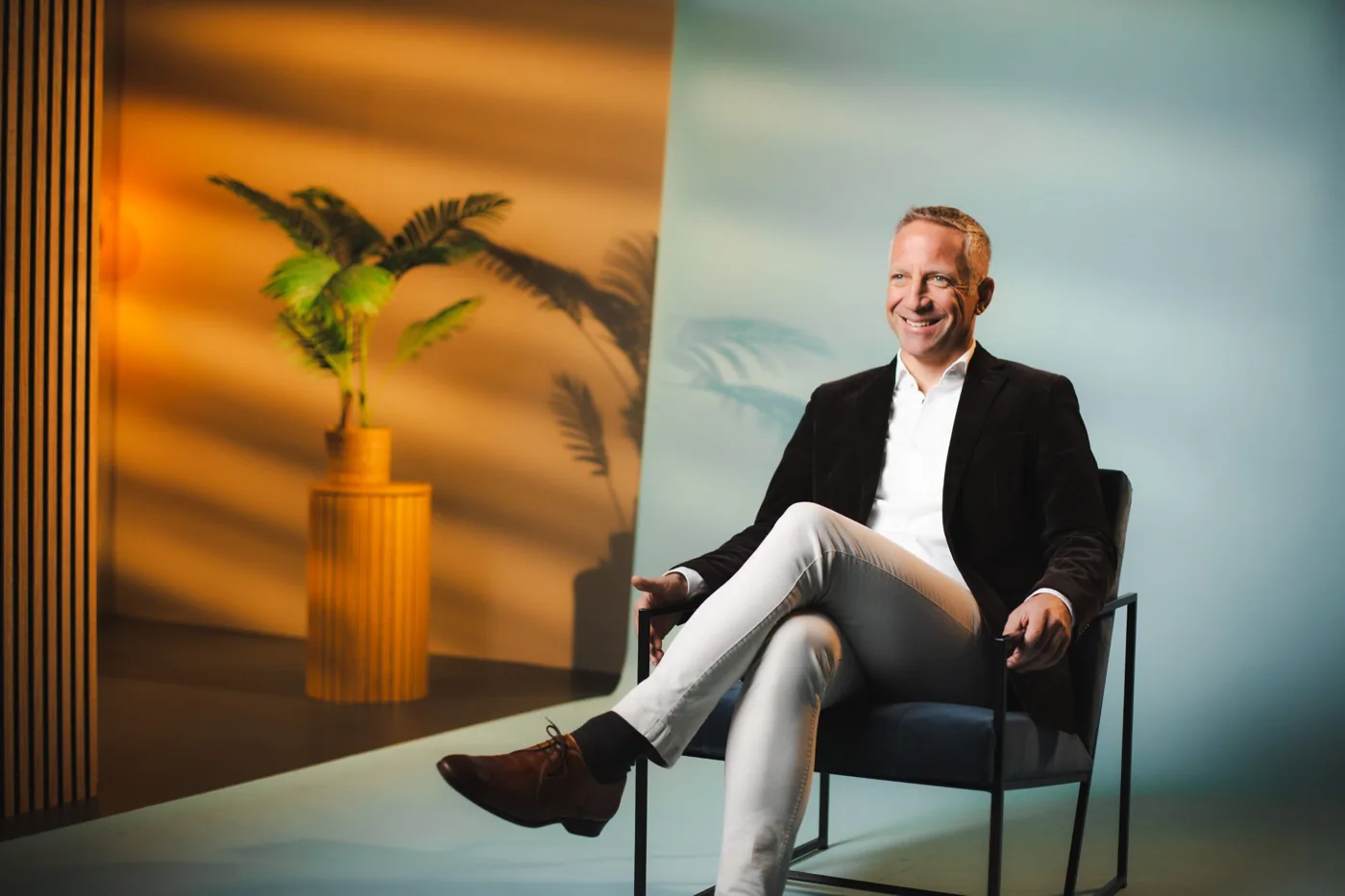 Interviewpartner lächelnd im Sessel auf einem farbig ausgeleuchteten Set